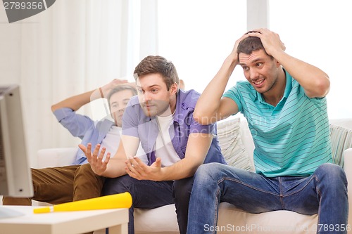 Image of sad male friends with vuvuzela watching sports