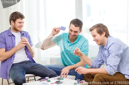 Image of happy three male friends playing poker at home