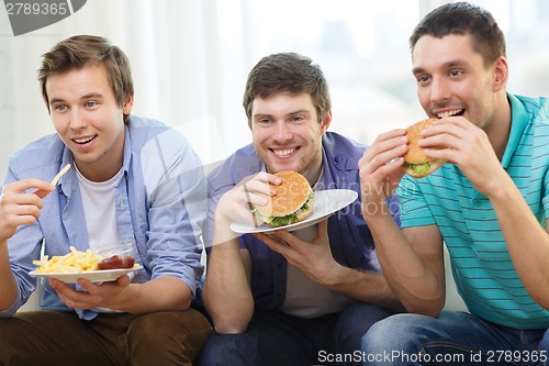 Image of smiling friends with soda and hamburgers at home