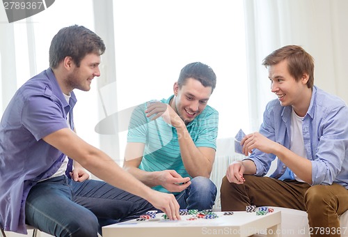 Image of happy three male friends playing poker at home