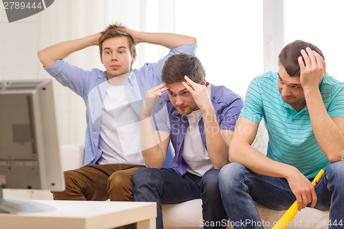 Image of sad male friends with vuvuzela watching sports