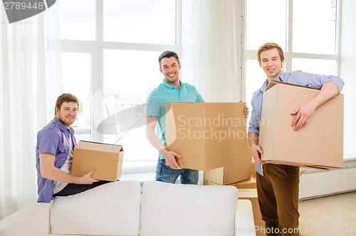 Image of smiling male friends carrying boxes at new place