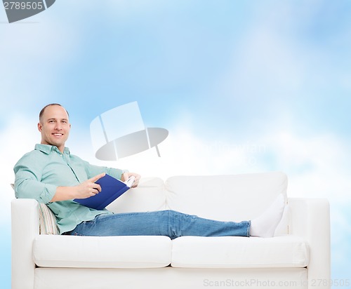 Image of smiling man lying on sofa with book