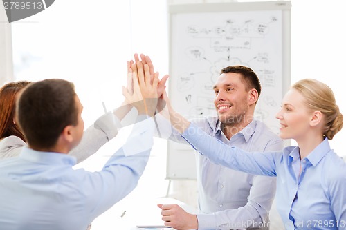 Image of happy business team giving high five in office