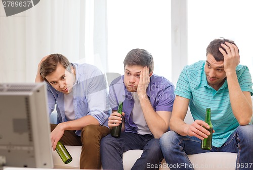 Image of sad male friends with beer watching sports