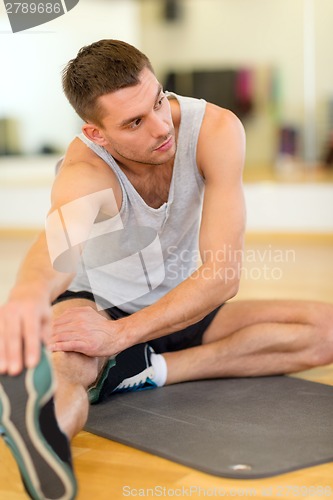 Image of serious man stretching on mat in the gym