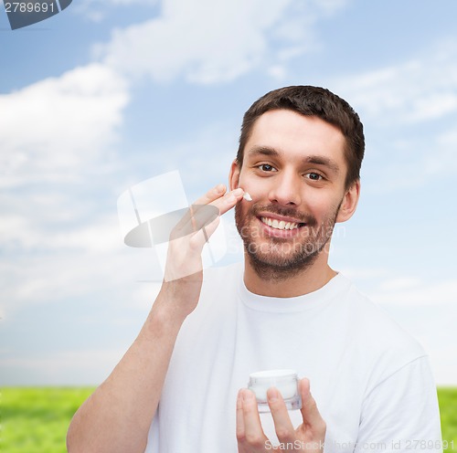 Image of beautiful smiling man applyin cream