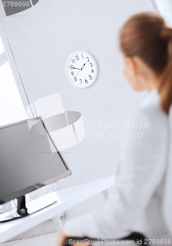 Image of businesswoman looking at wall clock in office