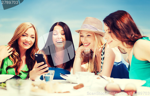 Image of girls looking at smartphone in cafe on the beach