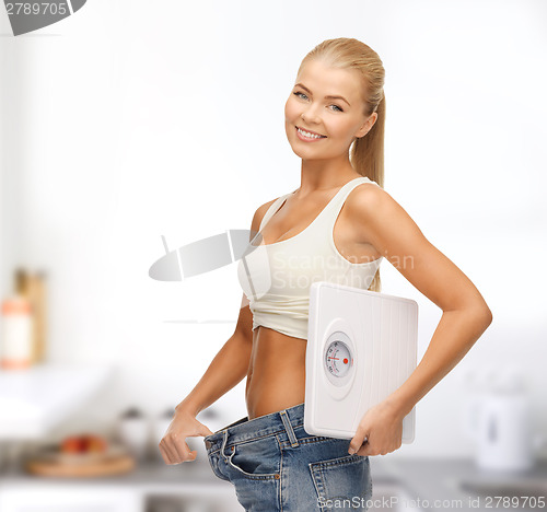 Image of smiling woman showing big pants and holding scales