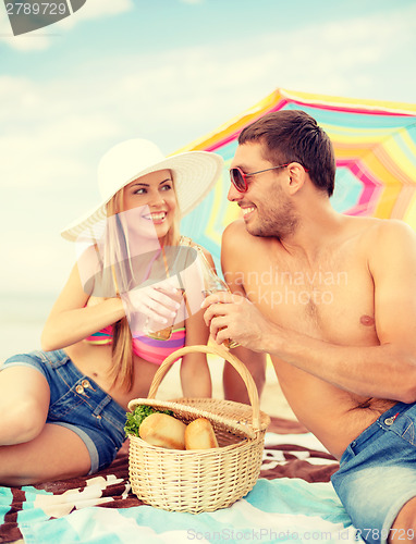 Image of smiling couple having picnic on the beach