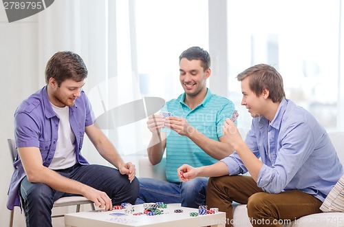 Image of happy three male friends playing poker at home