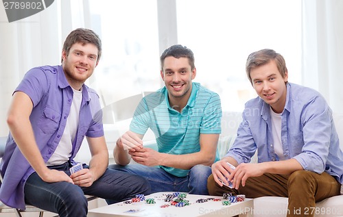 Image of happy three male friends playing poker at home