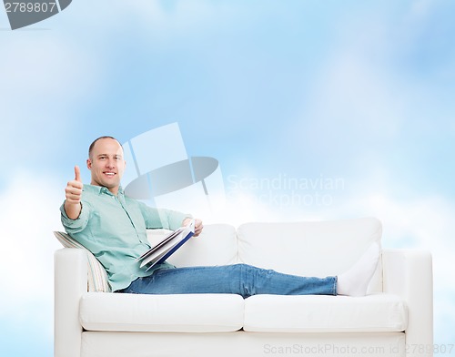 Image of smiling man lying on sofa with book