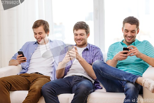 Image of smiling friends with smartphones at home