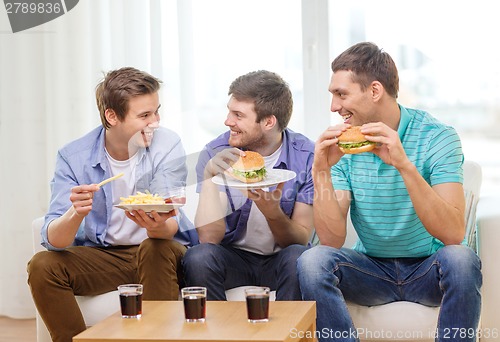 Image of smiling friends with soda and hamburgers at home