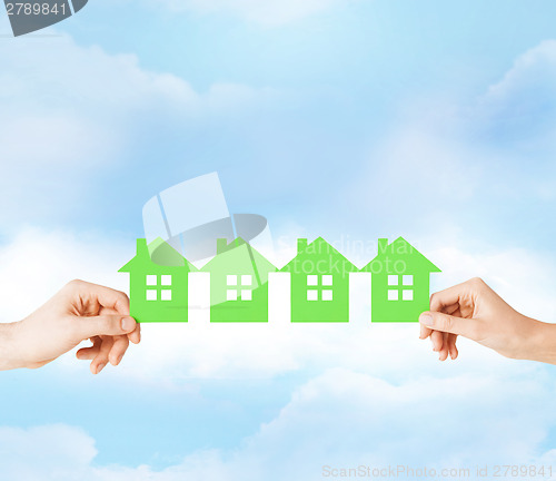 Image of man and woman hands with many green paper houses