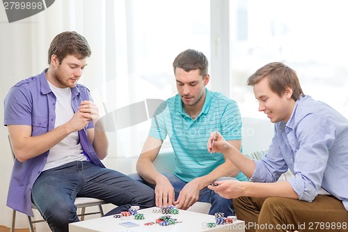 Image of happy three male friends playing poker at home