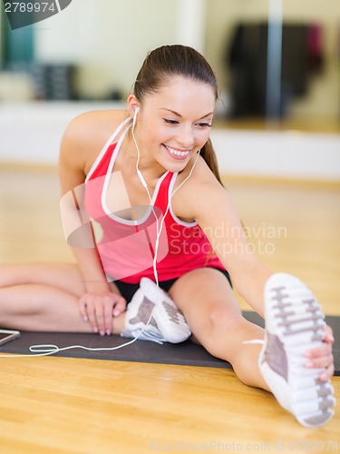 Image of smiling girl with smartphone and earphones in gym