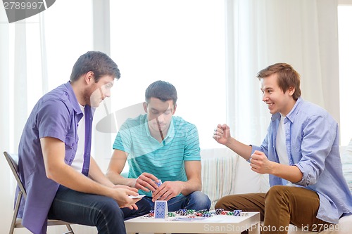 Image of happy three male friends playing poker at home