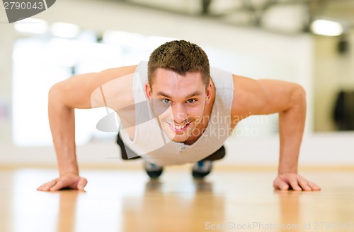 Image of smiling man doing push-ups in the gym