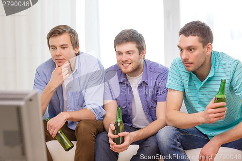 Image of happy male friends with beer watching tv at home