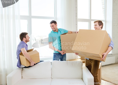 Image of smiling male friends carrying boxes at new place