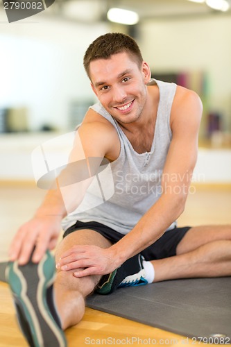 Image of smiling man stretching on mat in the gym