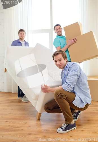 Image of smiling friends with sofa and boxes at new home