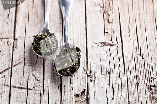 Image of two spoons of dried green tea leaves 