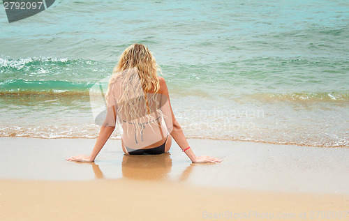 Image of The young girl sits by the sea near water.