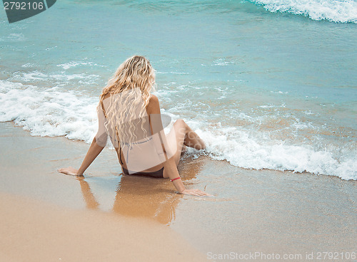 Image of The young girl sits by the sea near water.