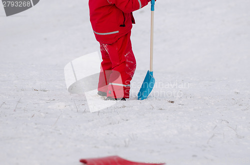 Image of child stand with snow shovel in waterproof wear 