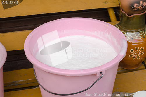 Image of pink bucket full of cow milk on wooden bench 