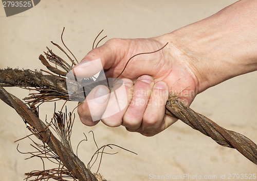 Image of Human hand compresses old steel cable