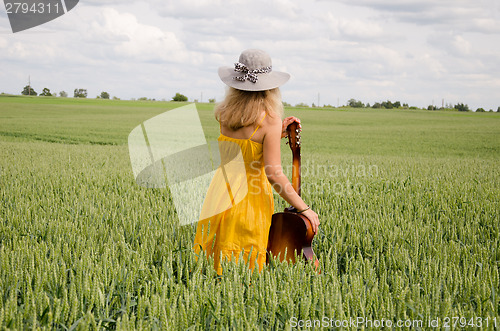 Image of back view of women with guitar in wide rye field  