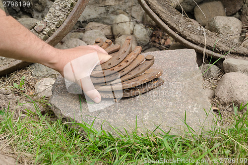 Image of man hand put iron horseshoe pile on stone outdoor 