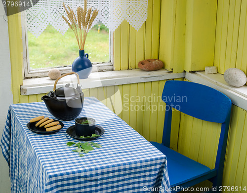 Image of teapot with tea cup and cookie on table blue chair 