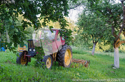 Image of tractor with harrow the garden apple trees in yard 
