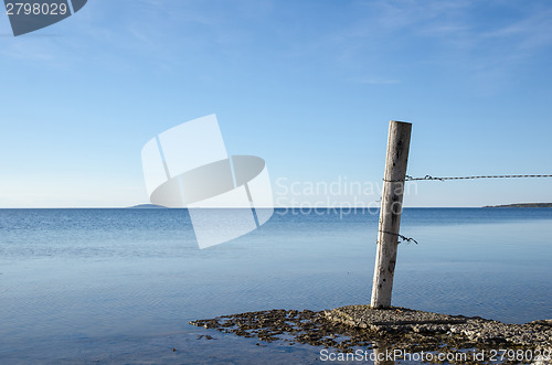 Image of Weathered old wooden pole by a flat rock coast