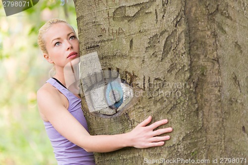 Image of Young woman hugging a tree.