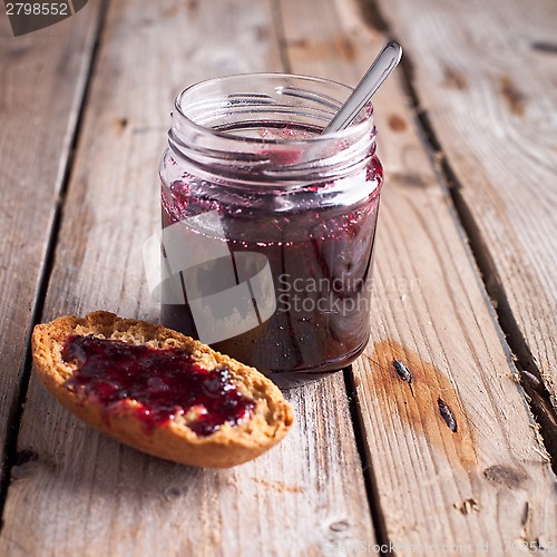 Image of black currant jam in glass jar and cracker