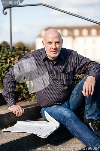 Image of Man sitting on steps reading a newspaper