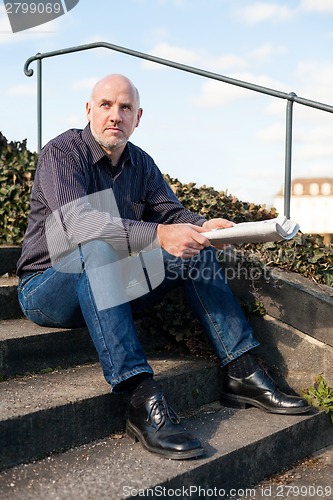 Image of Man sitting on steps reading a newspaper