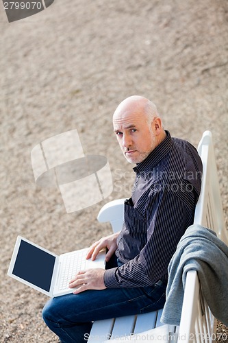 Image of Man sitting on a bench using a laptop