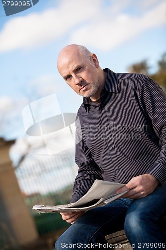 Image of Man sitting reading a newspaper on a stone wall