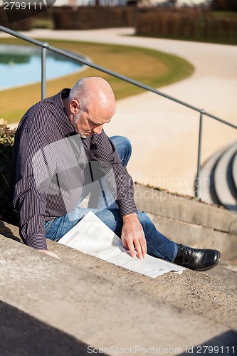 Image of Man sitting on steps reading a newspaper