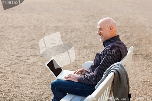 Image of Man sitting on a bench using a laptop
