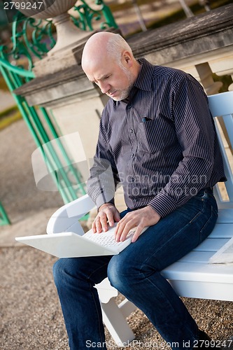 Image of Man sitting on a bench using a laptop