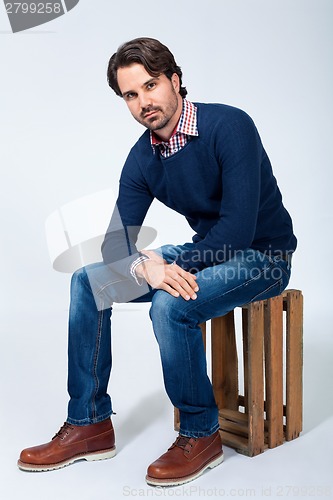 Image of Handsome young man sitting on a wooden box